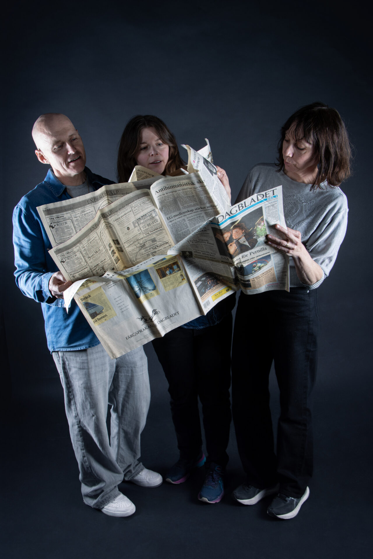 Foto på tre personer som tittar i en fiktiv tidning i tabloidformat