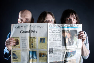 Foto på tre personer som tittar upp bakom en fiktiv tidning i tabloidformat